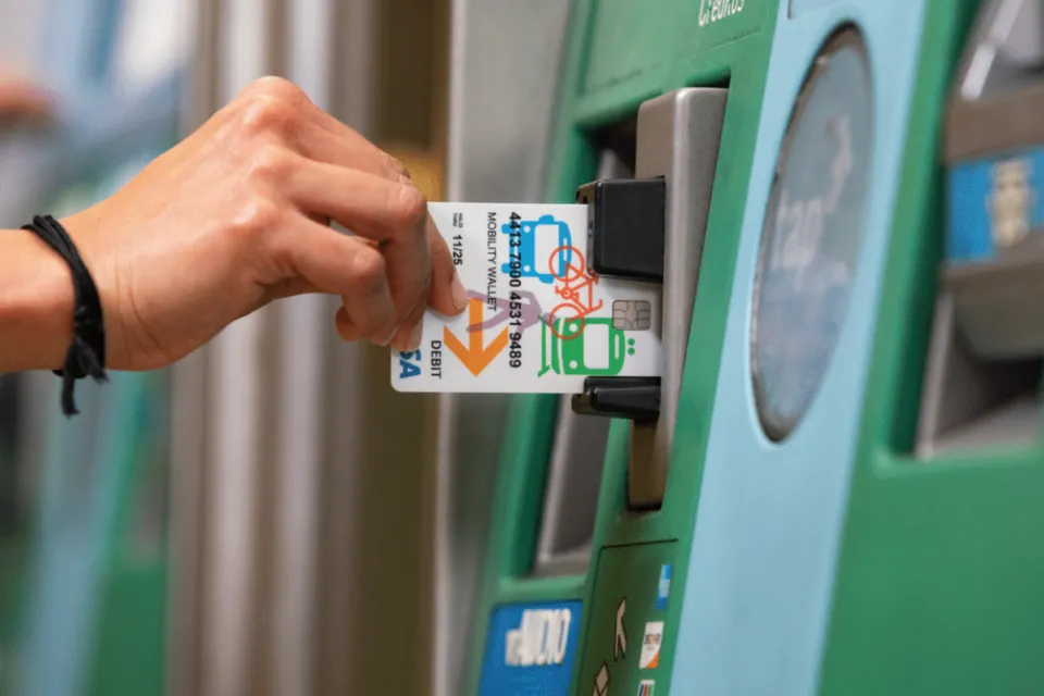 Close-up of hand inserting Mobility Wallet card into green Los Angeles Metro ticketing machine.